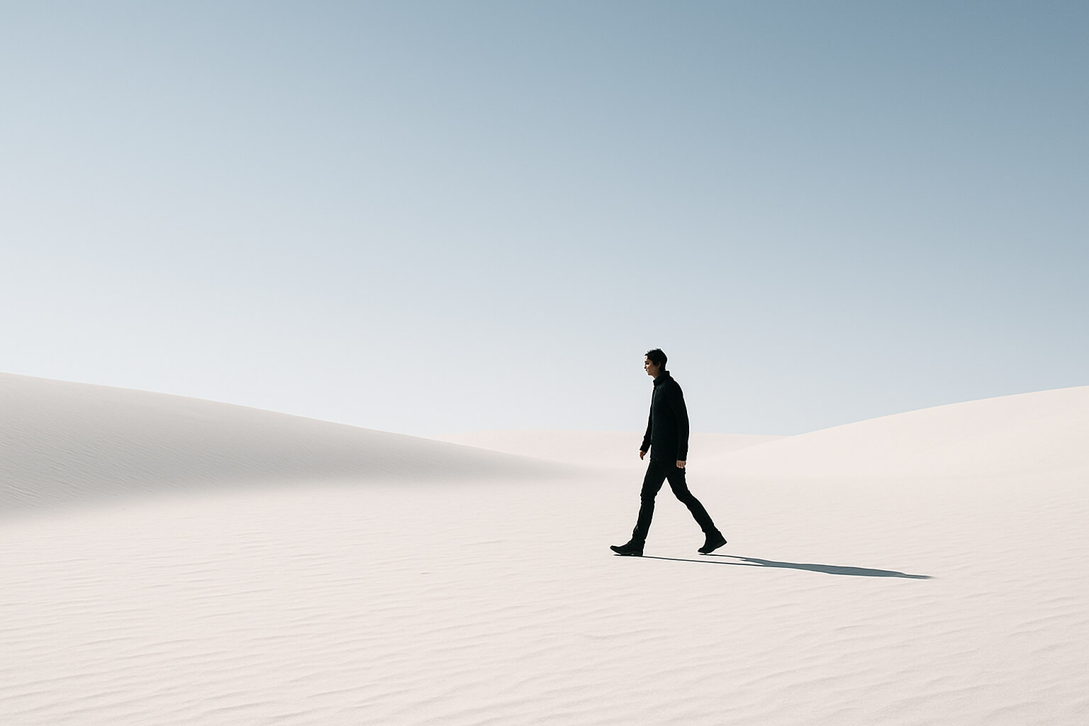 Minimalist photo of a person walking in a vast, empty landscape with clear negative space around them.