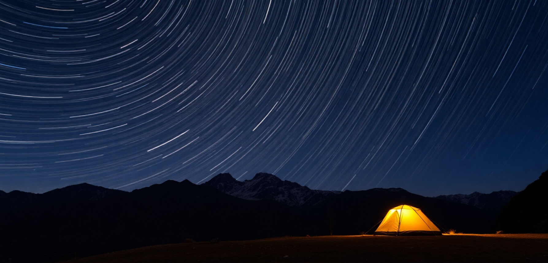Star trails forming circular patterns above a mountain at night with a lit tent in the foreground.